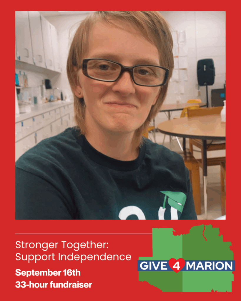 A young woman with short light brown hair and glasses smiles softly while sitting in a classroom with tables and chairs behind her. She wears a dark t-shirt with a green graduation cap graphic. The image is framed with a red border. Text at the bottom reads: “Stronger Together: Support Independence. September 16th | 33-hour fundraiser.” A green map of Marion County with the Give4Marion logo is displayed in the bottom right corner.