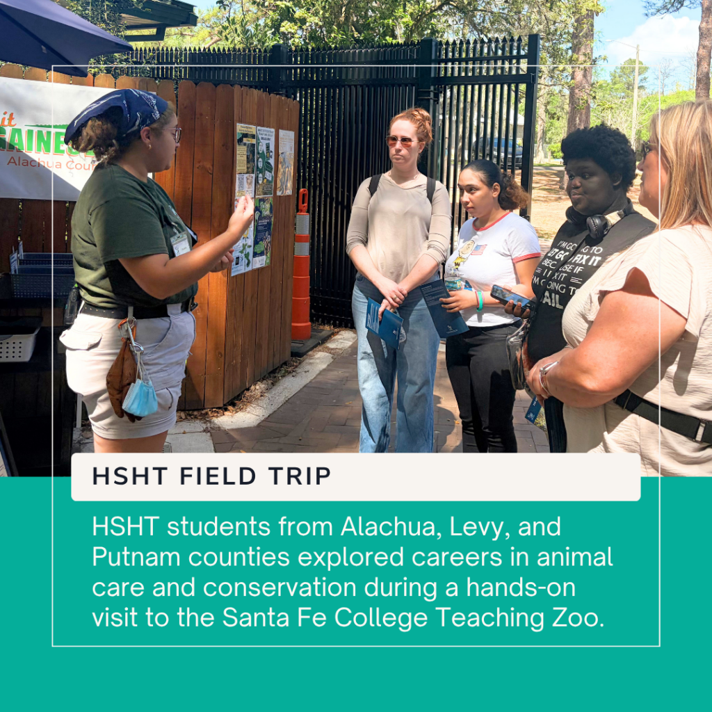 A group of High School High Tech (HSHT) students from Alachua, Levy, and Putnam counties listens attentively as a staff member from the Santa Fe College Teaching Zoo provides information during a guided tour. The students stand outdoors near the zoo entrance, holding informational materials while learning about careers in animal care, conservation, and zoo operations. A graphic overlay reads "HSHT Field Trip" and highlights the students' hands-on career exploration experience.
